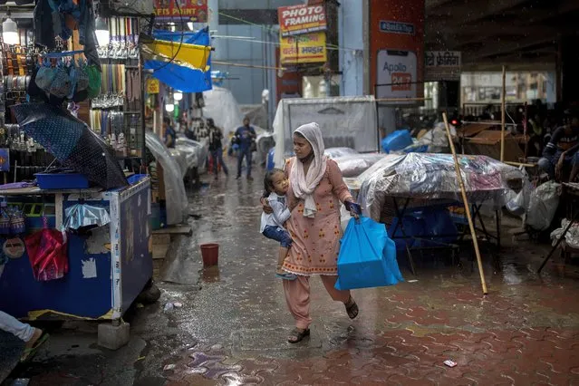 A woman carries a child as she hurriedly walks through a market during a downpour in Noida, a suburb of New Delhi, India, Friday, July 30, 2021. (Photo by Altaf Qadri/AP Photo)