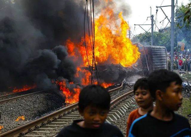 Children walk near a burning commuter train after it collided at Bintaro district in Jakarta, on December 9, 2013. Seven passengers died and at least 20 were injured after it collided with a truck loaded with gasoline. (Photo by Reuters/Beawiharta)