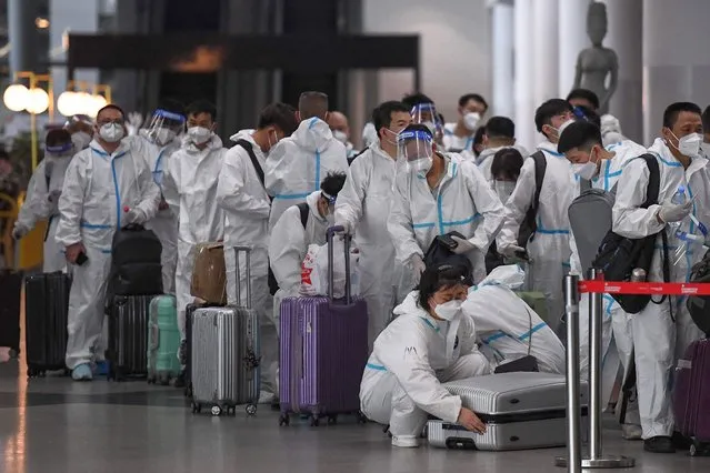 Travellers wearing hazmat suits wait in line to board a plane at Phnom Penh airport on November 14, 2022. (Photo by Nhac Nguyen/AFP Photo)