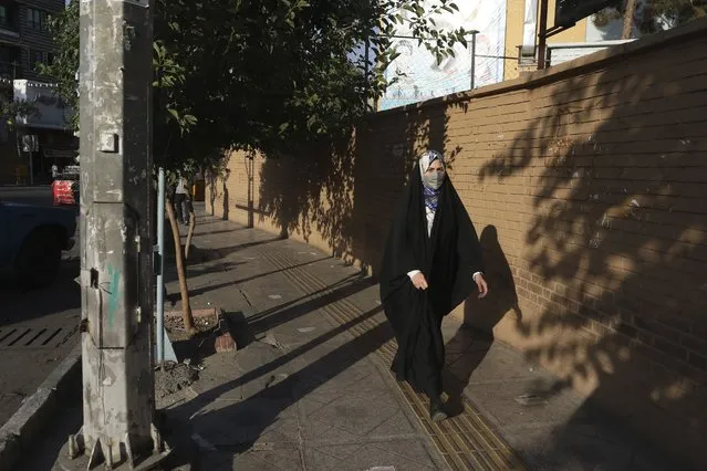 A woman wearing protective face mask to help prevent the spread of the coronavirus walks on a sidewalk in southern Tehran, Iran, Tuesday, July 20, 2021. (Photo by Vahid Salemi/AP Photo)