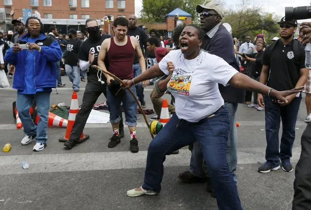Members of the community hold back a man (obscured by woman in white) who attempted to go after police officers after items were thrown and pepper spray was used outside a recently looted and burned CVS store in Baltimore, Maryland, United States April 28, 2015. (Photo by Jim Bourg/Reuters)