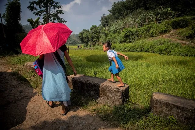 An Indian school girl playfully walks above roadside parapets as she returns home with her mother in Umwang village, along the Assam-Meghalaya state border, India, Wednesday, October 27, 2021. (Photo by Anupam Nath/AP Photo)