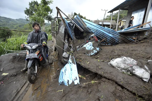 A motorist rides past the wreckage of a truck partially buried under the mud following a landslide in Songan village on Bali island, Indonesia, Friday, February 10, 2017. A number of people including young children were killed in the landslides on the tourist island that wiped out several homes, Indonesia's disaster mitigation agency said. (Photo by AP Photo)