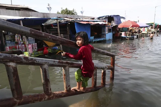 A young girl plays during a tidal flood at Muara Angke Port in Jakarta, Indonesia, Tuesday, November 9, 2021. Rising sea levels and rapid land subsidence due to over-extraction of groundwater have caused the capital city to sink at an average of 10 centimeters (4 inches) a year, making it one of the world's fastest sinking cities. (Photo by Tatan Syuflana/AP Photo)