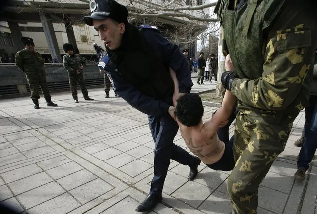 Members of Crimean self-defense units and Interior Ministry members detain a topless activist from Ukrainian feminist group Femen taking part in an anti-war protest near the Crimean parliament building in Simferopol March 6, 2014. (Photo by David Mdzinarishvili/Reuters)