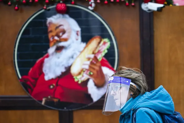 A woman wears a face shield as she walks past an image of Santa Claus at a Christmas market, in London, Thursday, December 16, 2021. The U.K. recorded the highest number of confirmed new COVID-19 infections Wednesday since the pandemic began, and England's chief medical officer warned the situation is likely to get worse as the omicron variant drives a new wave of illness during the Christmas holidays. The U.K. recorded 78,610 new infections on Wednesday, 16% higher than the previous record set in January. (Photo by Alberto Pezzali/AP Photo)