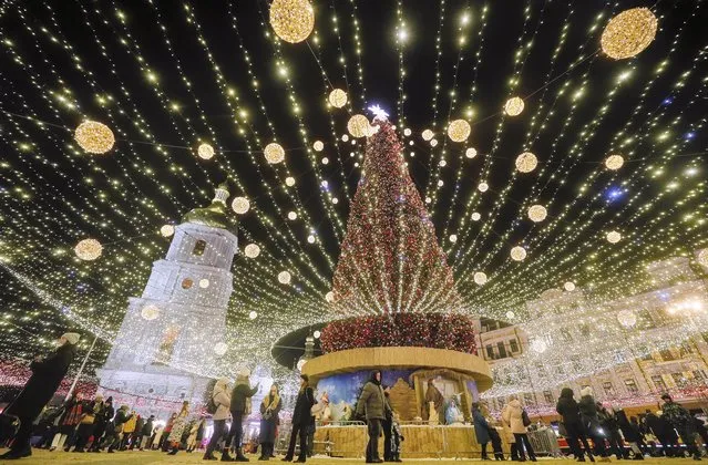 Ukrainians walk around the main Christmas Tree in front of the Saint Sophia's Cathedral in Kiev, Ukraine, 23 December 2021. The tree of 31 meters features more than ten thousand Christmas tree decorations. (Photo by Sergey Dolzhenko/EPA/EFE)