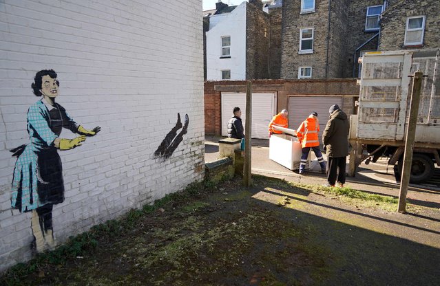 Workers remove a chest freezer that had formed part of an artwork, acknowledged to by street artist Banksy, from the side of a house in Margate, south east England on February 14, 2023. The artwork appears to show a a 1950s housewife with a swollen eye, missing a tooth, and apparently shutting a man in a freezer. The freezer was later removed by council workers. (Photo by William Edwards/AFP Photo)