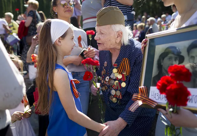 Olga Vasiljeva, an 93 -year-old veteran of World War II receives flowers at the Antakalnis memorial during Victory Day celebrations in Vilnius, Lithuania, Monday, May 9, 2015. (Photo by Mindaugas Kulbis/AP Photo)