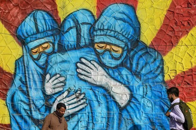 A pedestrian walks past a wall mural depicting health workers wearing Personal Protective Equipment (PPE) suits to spread awareness about the Covid-19 coronavirus in Mumbai on January 29, 2022. (Photo by Punit Paranjpe/AFP Photo)