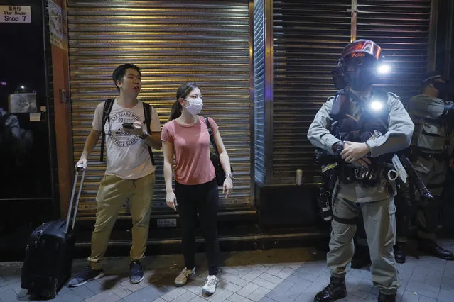 Pedestrians looks at Riot Police with face mask in the Tsim Sha Tsui district in Hong Kong, Thursday, October 10, 2019. A Hong Kong government official said on Thursday that Apple was responsible for removing a smartphone application which allowed activists to report police movements. (Photo by Kin Cheung/AP Photo)