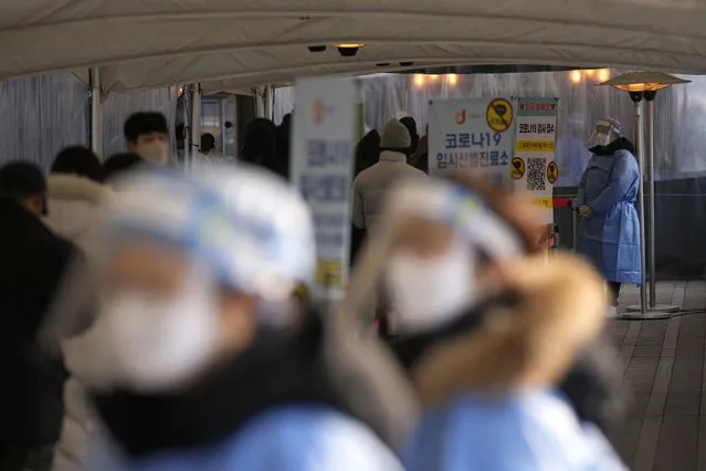 Health workers wearing protective gears stand to help visitors at a temporary screening clinic for the coronavirus near the Seoul City Hall in Seoul, South Korea, Wednesday, January 26, 2022. (Photo by Lee Jin-man/AP Photo)