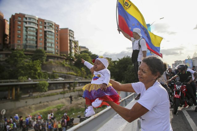 A supporter of presidential candidate Edmundo Gonzalez holds up a baby waiting for him and opposition leader Maria Corina Machado to pass by, during a closing election campaign rally in Caracas, Venezuela, July 25, 2024. (Photo by Cristian Hernandez/AP Photo)