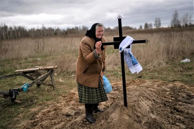 Nadiya Trubchaninova, 70, cries while holding the cross of her son Vadym, 48, who was killed by Russian soldiers last March 30 in Bucha, during his funeral in the cemetery of Mykulychi, on the outskirts of Kyiv, Ukraine, Saturday, April 16, 2022. After nine days since the discovery of Vadym's corpse, finally Nadiya could have a proper funeral for him. This is not where Nadiya Trubchaninova thought she would find herself at 70 years of age, hitchhiking daily from her village to the shattered town of Bucha trying to bring her son's body home for burial. (Photo by Rodrigo Abd/AP Photo)