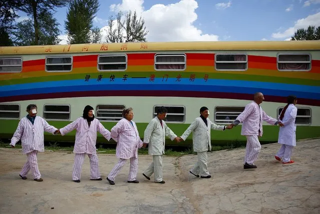 A nurse (R) leads cataract patients as they walk past a train which serves as a mobile hospital, in Ledu county, Qinghai province, China, July 23, 2015. The train, donated by people from Hong Kong and Macau, came to the county three months ago and has provided free medical treatment to over 900 local cataract patients, local media reported. (Photo by Simon Zo/Reuters)