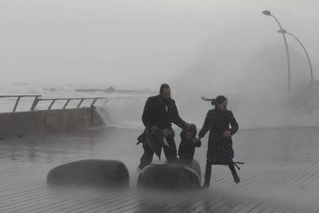 A family runs from large waves during a stormy day at the port of Tel Aviv, Israel, 26 December 2019. (Photo by Abir Sultan/EPA/EFE)