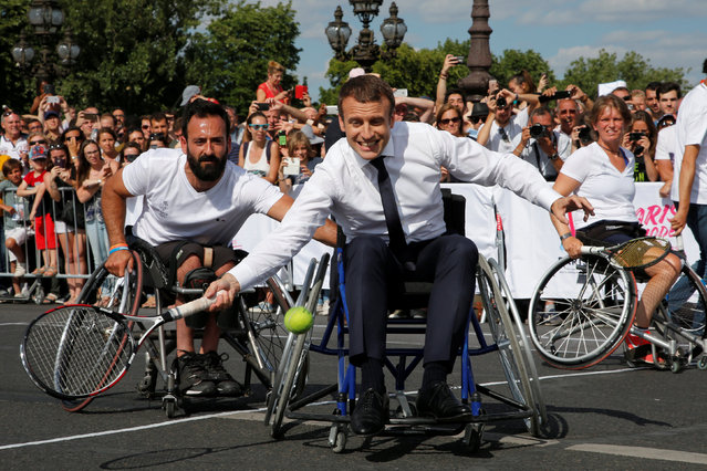 French President Emmanuel Macron returns the ball while sitting in a wheelchair as he plays tennis on the Pont Alexandre III in Paris, France, June 24, 2017. The French capital is transformed into a giant Olympic park to celebrate International Olympic Days with a variety of sporting events for the public across the city during two days as the city bids to host the 2024 Olympic and Paralympic Games. (Photo by Jean-Paul Pelissier/Reuters)