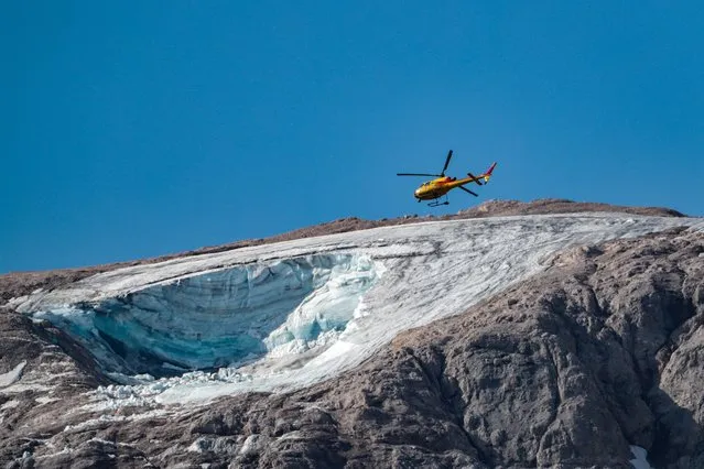 A rescue helicopter flies on July 4, 2022 over the glacier that collapsed the day before on the mountain of Marmolada, the highest in the Dolomites, one day after a record-high temperature of 10 degrees Celsius (50 degrees Fahrenheit) was recorded at the glacier's summit. Rescuers resumed the search for survivors today after an avalanche set off by the collapse of the glacier, the largest in the Italian Alps, killed at least six people and injured eight others. (Photo by Pierre Teyssot/AFP Photo)