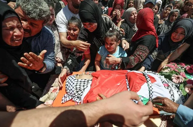 Family members mourn over the flag-draped body of Amjad Nashaat Abu Alia, 16, who was killed a day earlier in clashes with Israeli security forces, during his funeral in the village of Al-Mughayer, east of the occupied West Bank city of Ramallah, on July 30, 2022. About 300 Palestinians had gathered yesterday for a protest march against Israeli settlement expansion in the area. Clashes erupted when Israeli settlers and Palestinians began throwing rocks at each other. (Photo by Abbas Momani/AFP Photo)