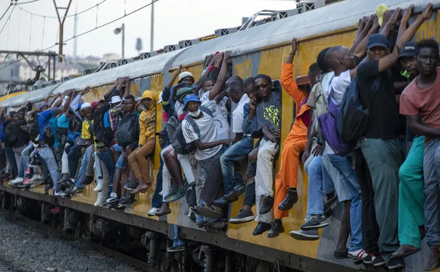 Train commuters hold on to the side of an overcrowded passenger train in Soweto, South Africa, Monday, March 16, 2020. South Africa will revoke nearly 10,000 visas issued this year to people from China and Iran, and visas will now be required for other high-risk countries that had been visa-free, including Italy and the United States. For most people, the new coronavirus causes only mild or moderate symptoms. For some it can cause more severe illness, especially in older adults and people with existing health problems. (Photo by Themba Hadebe/AP Photo)