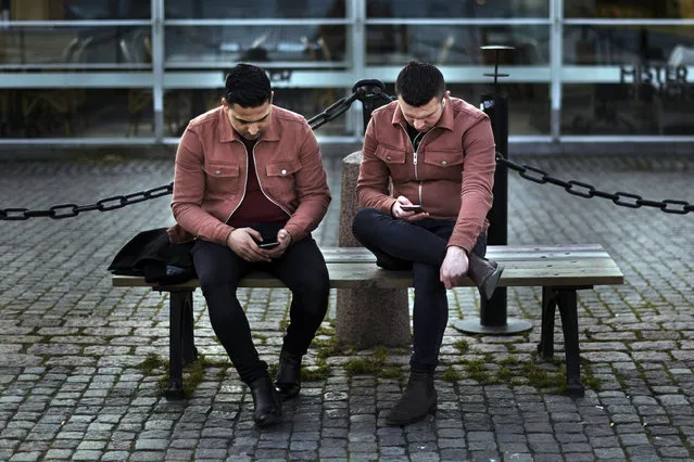 Two men check their phones as they sit near the harbor in Stockholm, Sweden, Wednesday, April 8, 2020. Swedish authorities have advised the public to practice social distancing because of the coronavirus pandemic, but still allow a large amount of personal freedom, unlike most other European countries. (Photo by Andres Kudacki/AP Photo)