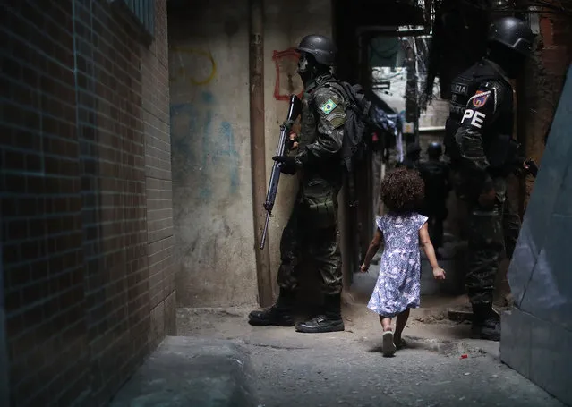A girl walks past Brazilian soldiers standing on patrol in the Rocinha “favela” community on September 25, 2017 in Rio de Janeiro, Brazil. The Brazilian Army and other armed forces entered the favela on September 22 in an ongoing operation following firefights involving drug gangs in the favela, which is one of the largest in Latin America. Rio has suffered an uptick in violence following the Rio 2016 Olympic Games. (Photo by Mario Tama/Getty Images)