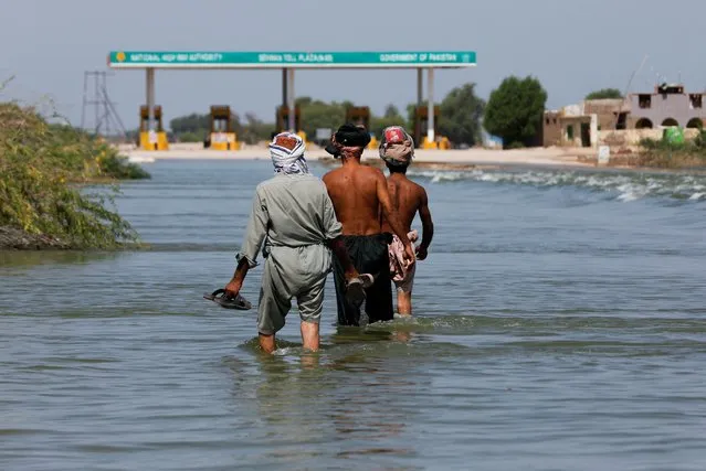 Displaced people walk on flooded highway, following rains and floods during the monsoon season in Sehwan, Pakistan, September 16, 2022. (Photo by Akhtar Soomro/Reuters)
