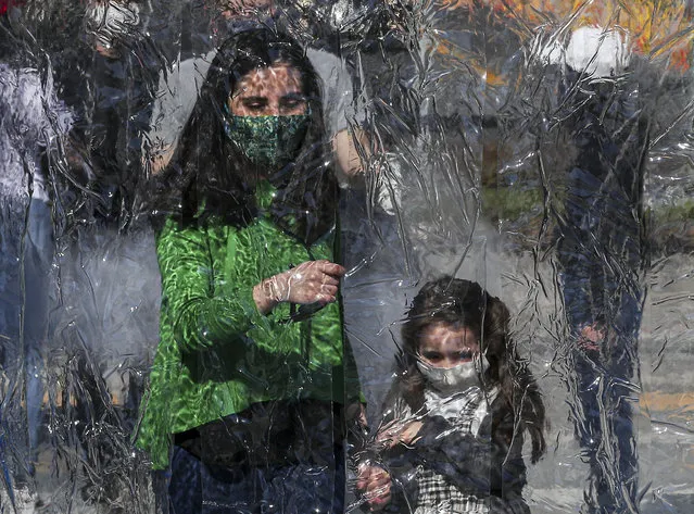A woman and child wearing protective face masks prepare to enter a decontamination chamber as a precaution against the spread of the new coronavirus, at the entrance of Araucano Park in Las Condes borough of Santiago Chile, Wednesday, July 29, 2020. As the Chilean government put a roadmap in place to roll back quarantine measures, various neighborhoods in the capital started on Tuesday to ease the COVID-19 lockdown. (Photo by Esteban Felix/AP Photo)
