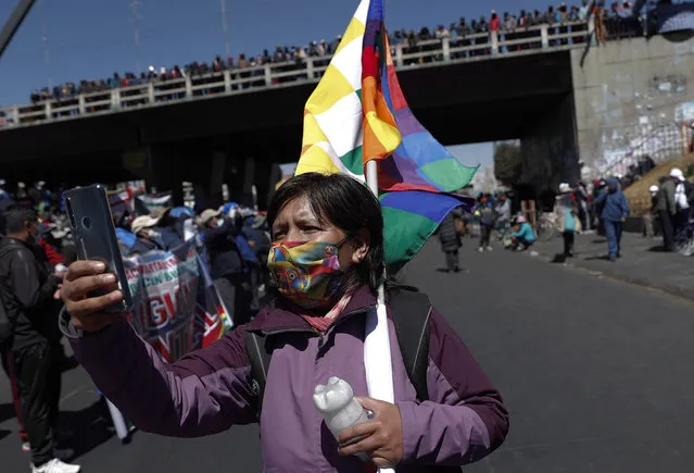 A woman wearing a mask amid the COVID-19 pandemic takes a photo with her cell phone during a protest against the postponement of the presidential election in El Alto, Bolivia, Thursday, August 13, 2020. Citing the ongoing new coronavirus pandemic, Bolivia's highest electoral authority delayed presidential elections from Sept. 6 to Oct. 18, the third time the vote has been delayed. (Photo by Juan Karita/AP Photo)