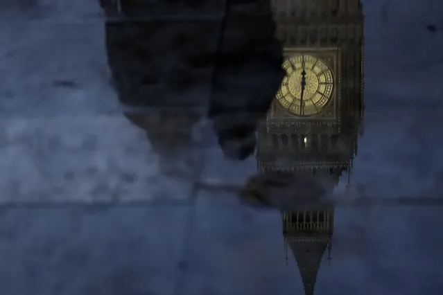 Commuters are reflected in a puddle with the Queen Elizabeth Tower in the background which contains the bell known as 'Big Ben, part of the Palace of Westminster, following a rain shower in London, Thursday, October 20, 2022. British Prime Minister Liz Truss resigned Thursday, bowing to the inevitable after a tumultuous, short-lived term in which her policies triggered turmoil in financial markets and a rebellion in her party that obliterated her authority. (Photo by Alastair Grant/AP Photo)