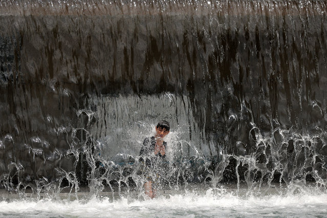 A child stands beneath the waterfall while taking a break from the heat in the Yards Park Canal Basin on July 17, 2025 in Washington, DC. The nation's capital is under a heat advisory with temperatures reaching the mid-90s and the heat index climbing over 100-degrees Fahrenheit. (Photo by Chip Somodevilla/Getty Images)
