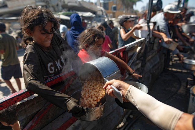 Palestinians, including children, hold pots as they queue to receive food from a kitchen that provides free food for displaced people in Gaza City, northern Gaza Strip, 12 September 2025. According to the UN, around 90 percent of the population, or 1.9 million people, in Gaza have been displaced since the start of the conflict. (Photo by Haitham Imad/EPA)