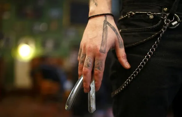 Alex “Torreto” Vellios, a 26-year old barber sports his tattoo of an open razor as he holds a real razor while preparing for his first customer of the day at his Torreto barber shop in Frankfurt, January 6, 2015. (Photo by Kai Pfaffenbach/Reuters)