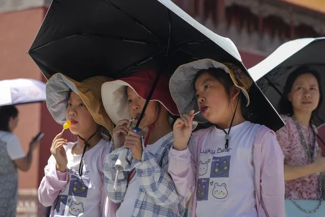 Children wearing sun hats and carrying an umbrella pose for a souvenir photo near the Forbidden City on a sweltering day in Beijing, Friday, July 7, 2023. (Photo by Andy Wong/AP Photo)