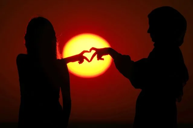 Girls make a heart sign as the sun sets over the Mediterranean Sea coastline in Beirut, Lebanon, Friday, July 14, 2023. (Photo by Hassan Ammar/AP Photo)