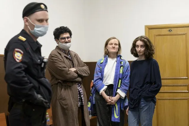 DOXA magazine editors from left, Armen Aramyan, Natalya Tyshkevich and Alla Gutnikova wait for a court session as a police officer, left, stands next in Moscow, Russia, Wednesday, April 14, 2021. Russian authorities levied criminal charges Wednesday against four young editors of an online student magazine that had coverage about the nationwide protests supporting jailed opposition leader Alexei Navalny earlier this year. (Photo by Denis Kaminev/AP Photo)
