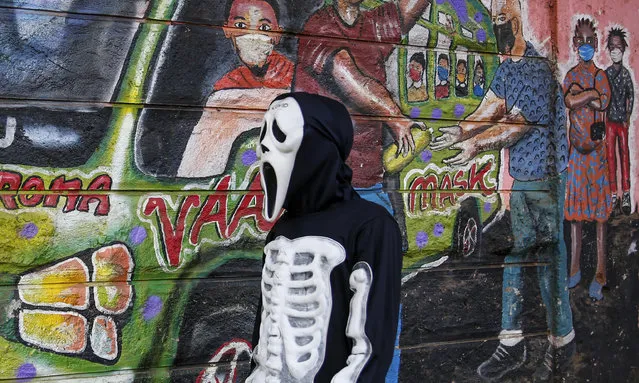 James Kiriva, 35, who took the initiative to educate his community about the importance of taking precautions to curb the spread of the coronavirus and COVID-19, walks around dressed as a skeleton to spread his message, past an informational mural, in the Kibera low-income neighborhood of Nairobi, Kenya Tuesday, April 13, 2021. (Photo by Brian Inganga/AP Photo)