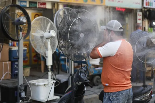A man cools off with a mist dispenser set up on al-Jumhuriya street in central Baghdad amid soaring temperatures, on July 23, 2023. (Photo by Ahmad Al-Rubaye/AFP Photo)