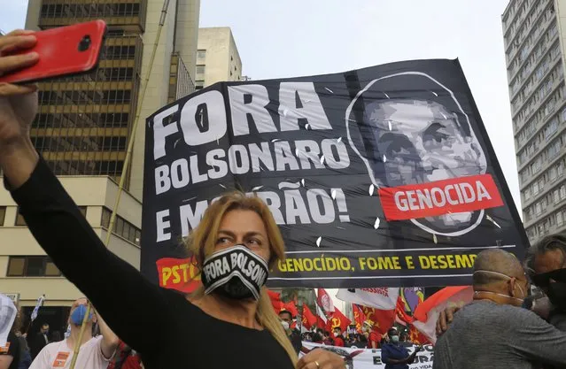 A woman takes a selfie backdropped by a banner depicting Brazilian President Jair Bolsonaro and a message that reads in Portuguese, “Get out Bolsonaro!” during a protest demanding Bolsonaro resign, in Sao Paulo, Brazil, Saturday, July 3, 2021. Activists called for nationwide demonstrations against Bolsonaro, gathering protestors to demand his impeachment amid allegations of potential corruption in the Health Ministry’s purchase of COVID-19 vaccines. (Photo by Nelson Antoine/AP Photo)