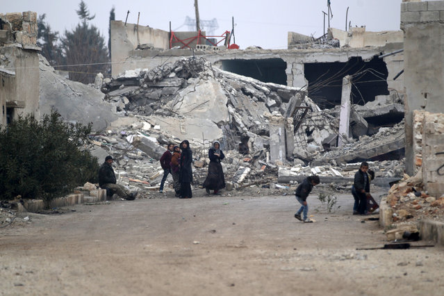 People stand near near rubble of damaged buildings in al-Rai town, northern Aleppo countryside, Syria December 25, 2016. (Photo by Khalil Ashawi/Reuters)