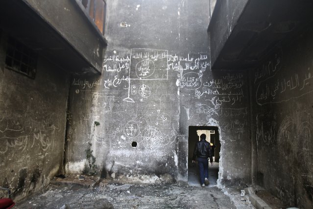 A man walks inside a damaged building with an Islamic flag drawn on the wall in the besieged town of Arbeen in the eastern Ghouta of Damascus January 17, 2015. The text on the wall reads: “Al-Qaeda's Jihad on the land of Sham, Al-Nusra front for the people of Sham, a project for the slaughter of Nasiriyah and infidels”. (Photo by Yaseen Al-Bushy/Reuters)