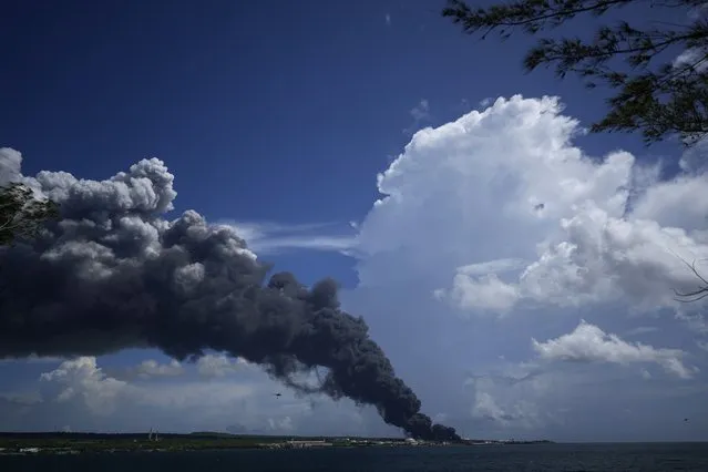 A huge plume of smoke rises from the Matanzas Supertanker Base, as firefighters work to quell a blaze which began during a thunderstorm the night before, in Matazanas, Cuba, Saturday, August 6, 2022. Cuban authorities say lightning struck a crude oil storage tank at the base, causing a fire that led to four explosions which injured more than 50 people. (Photo by Ramon Espinosa/AP Photo)
