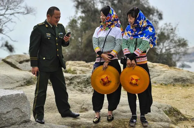 A People's Liberation Army officer looks at his phone as he speaks with two Hui'an maiden tourist guides in Hui'an county, Fujian, on December 9, 2013. (Photo by Reuters)
