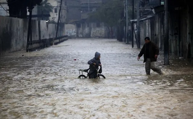 A man helps a boy out of a flooded street following heavy rains in Gaza City, on December 14, 2013. Hundreds of houses were flooded following a rain storm in Gaza. (Photo by Adel Hana/Associated Press)