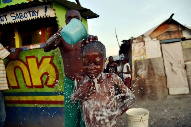 Beloni (34) gives a bath to his son, 6, on a small street in the neighborhood of Cite Vincent, on March 21, 2016 in the commune of Cite Soleil in the Haitian capital Port-au-Prince. World Water Day, marked on March 22, 2016, is an international observance to learn more about water related issues and to take action for sustainable management of freshwater resources. (Photo by Hector Retamal/AFP Photo)