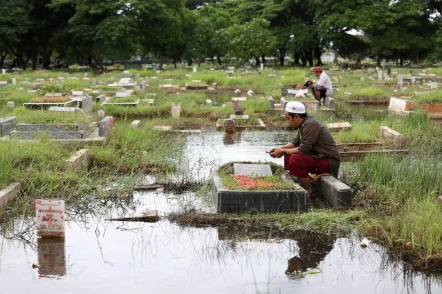 Men pray while visiting their relative's graves submerged in water due to heavy rain ahead of the holy fasting month of Ramadan, at the Semper cemetery complex in North Jakarta, Indonesia, on March 8, 2024. (Photo by Ajeng Dinar Ulfiana/Reuters)