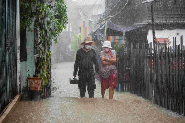 Koh Kret residents walk through a submerged alley during a heavy rainfall in Thailand on October 3, 2021. Twenty provinces have been affected by the Dianmu storm. Each day the riverside communities in Nonthaburi face renewed flooding. (Photo by Varuth Pongsapipatt/SOPA Images/LightRocket via Getty Images)