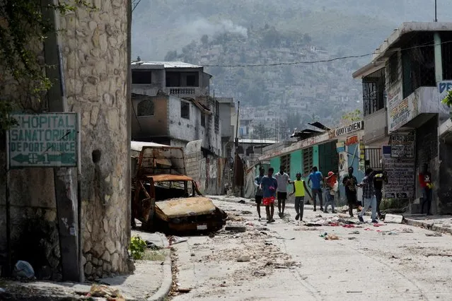 People walk past a damaged car in the Carrefour Feuilles neighborhood, which was deserted due to gang violence, in Port-au-Prince, Haiti on March 19, 2024. (Photo by Ralph Tedy Erol/Reuters)