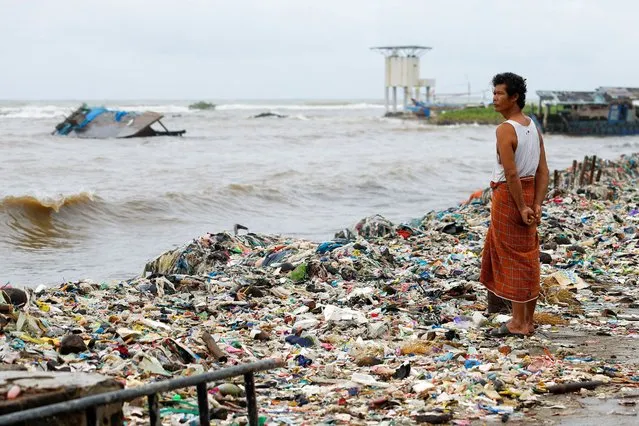 A man stands near trash, mostly plastics and domestic waste, on a beach in Teluk fishing village, as high tides brought by erratic weather sweeps trash to the shore, in Pandeglang regency, Banten province, Indonesia, on March 15, 2024. (Photo by Willy Kurniawan/Reuters)
