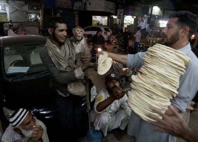 A Pakistani man who owns a monkey and others receive free bread distributed in Karachi, Pakistan, Monday, March 21, 2016. (Photo by Shakil Adil/AP Photo)